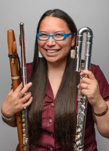 A woman smiles while holding several types of flute