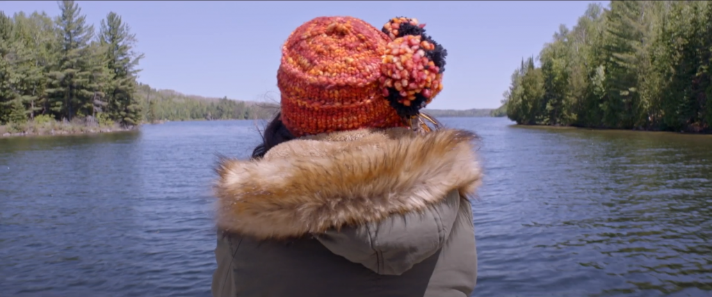 Rear view of a person, wearing a wool hat and a parka, as they look out over water