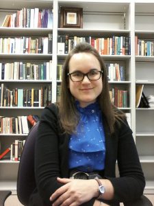 A woman in glasses in front of a bookcase.