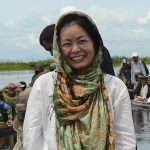 A woman smiles with a body of water in the background
