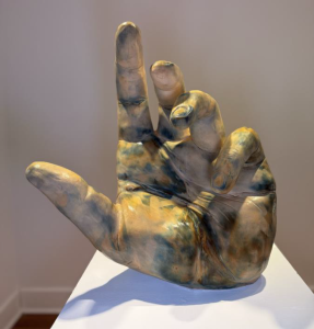 Ceramic model of a hand, facing the palm. The index finger is pointed up, while the pinky and ring fingers are curled in.