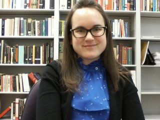 A woman in glasses in front of a bookcase.